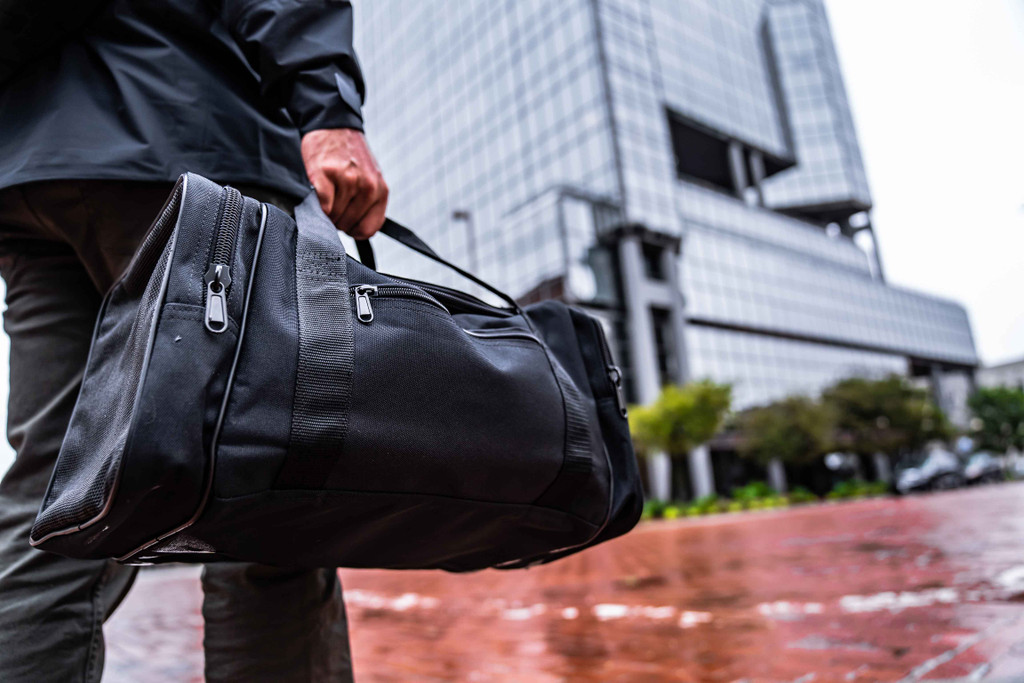 Black Square Sports Duffel carried by top handles in the city.